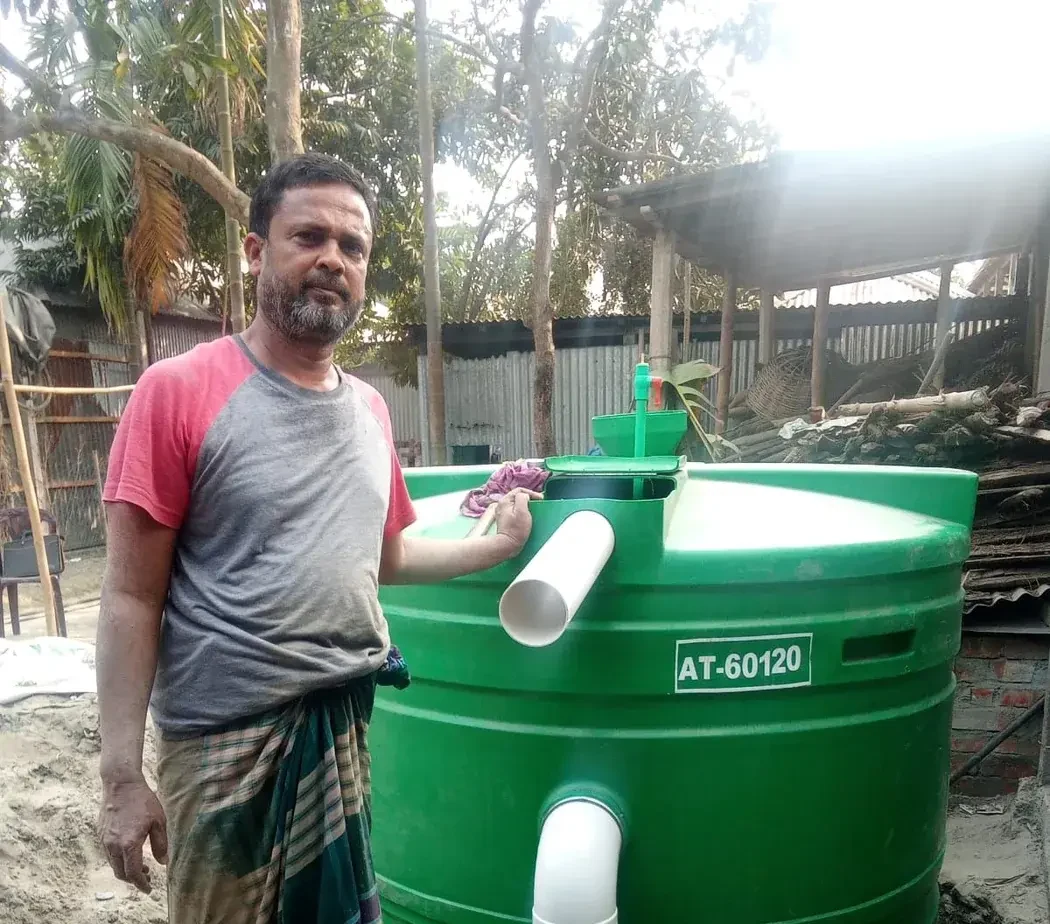 A household participant standing beside a Green Flame biogas digester in Bogra