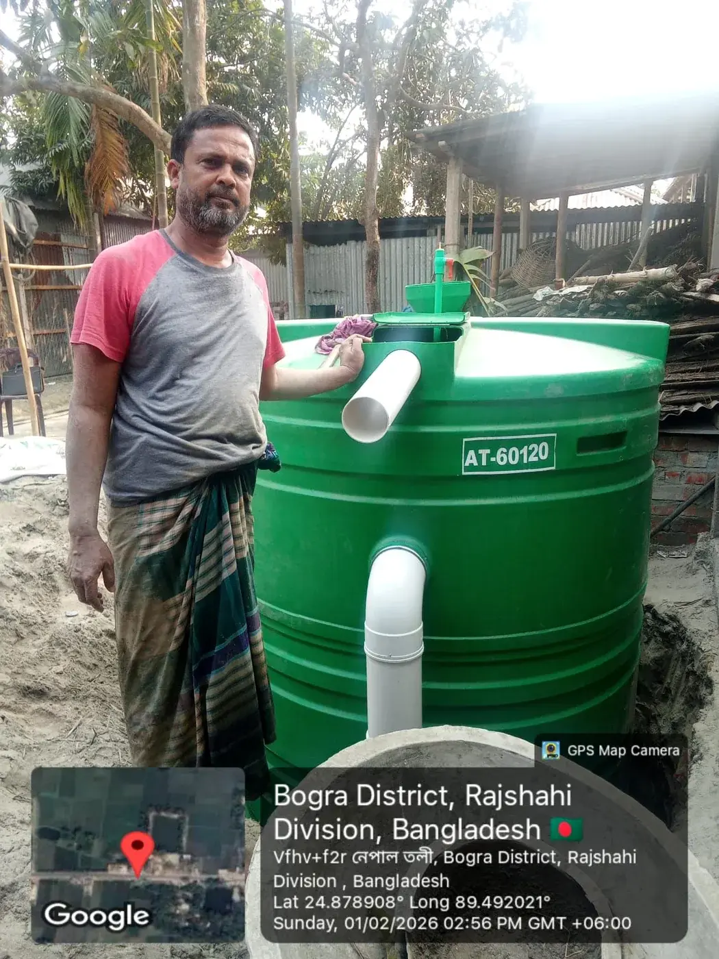 Man standing beside a green household biodigester in Bogra District