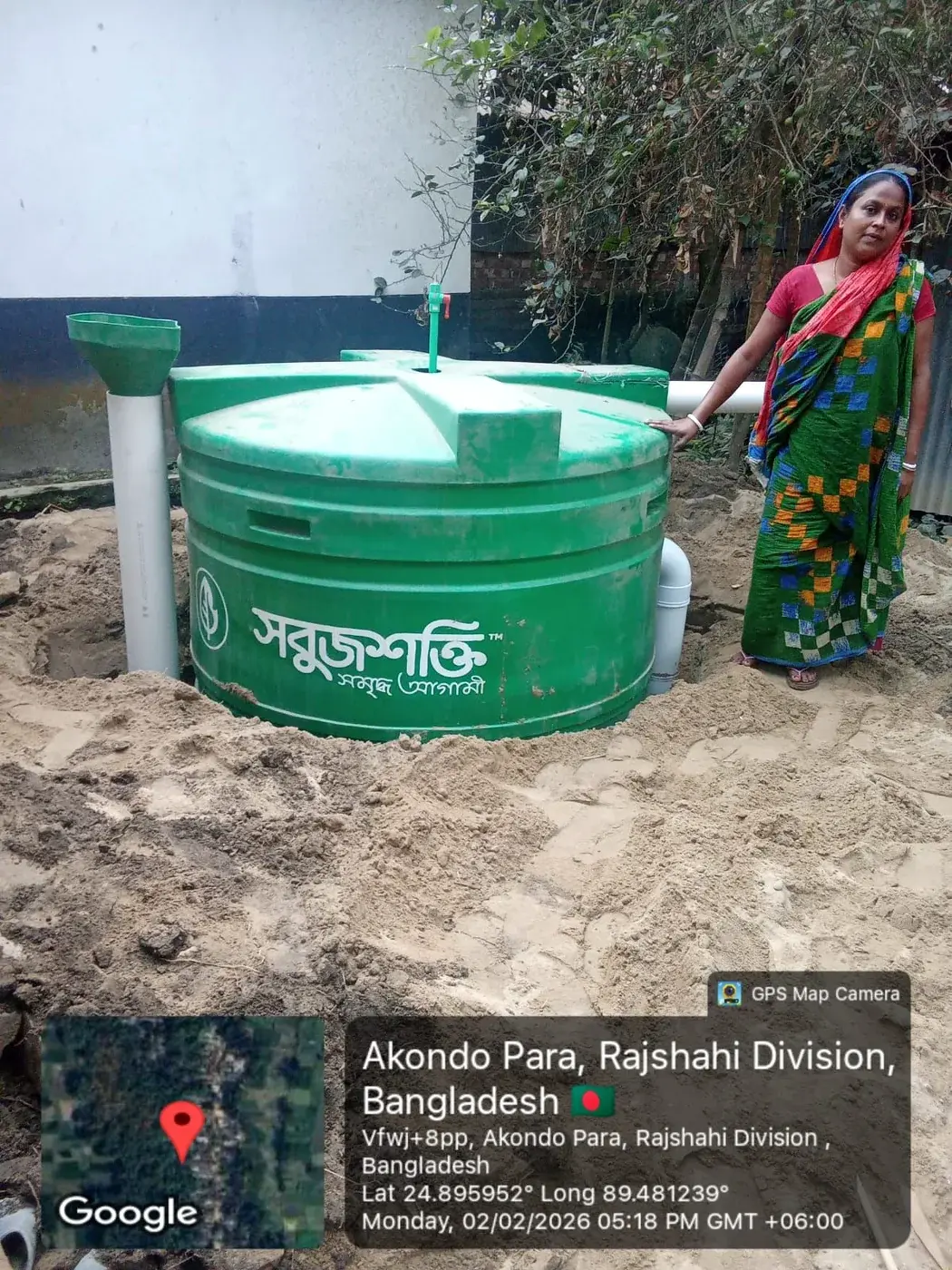 Woman standing beside a green household biodigester