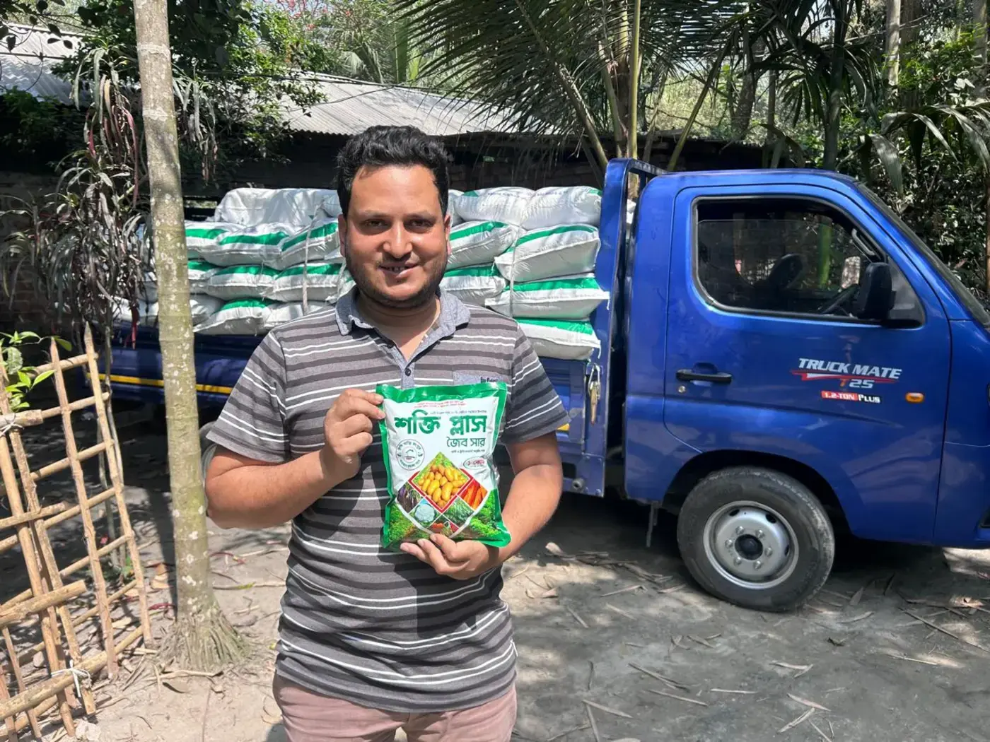 A project-linked enterprise representative holding a packaged organic fertiliser product beside a loaded vehicle
