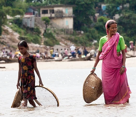 A woman and child moving through floodwater in a rural settlement